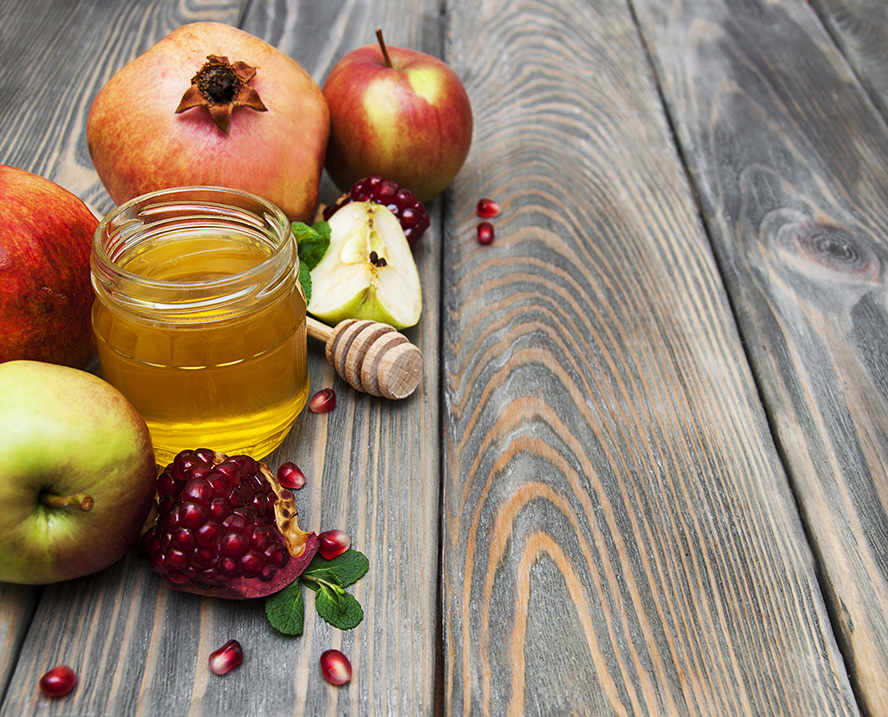 عکس با کیفیت طرح یا پوستر شب یلدا چند سیب و انار زیبا در کنار انار و سیب اسلایس شده و ظرف شیشه ای عسل به همراه قاشق چوبی عسل خوری در کنار میوه ها بر روی میز چوبی