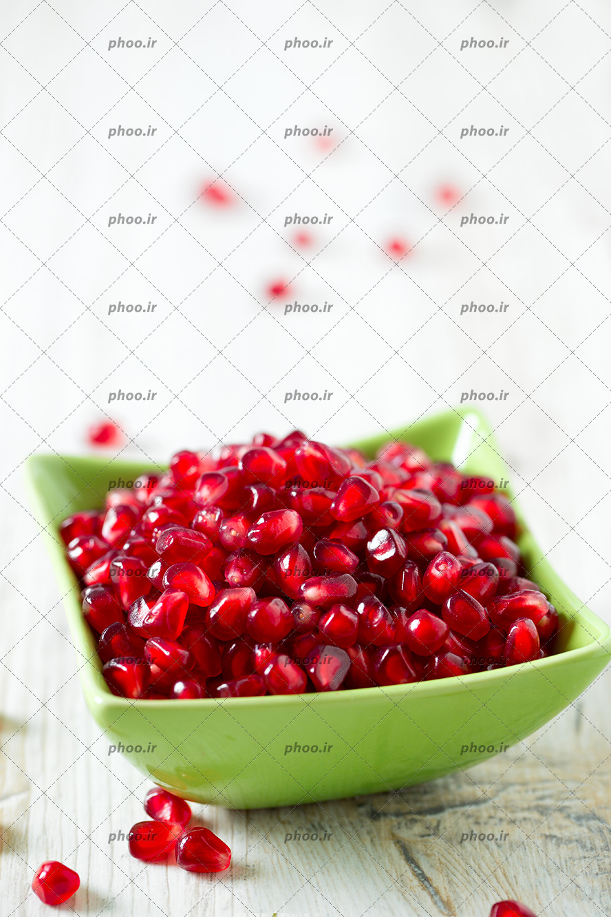 عکس با کیفیت دانه های قرمز انار داخل پیاله ی سبز بر روی میز از نمای نزدیک