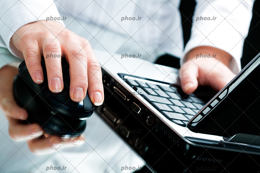 عکس یک آقا در حال کار با لپ تاپ و موس و انعکاس دست و موس روی شیشه میز