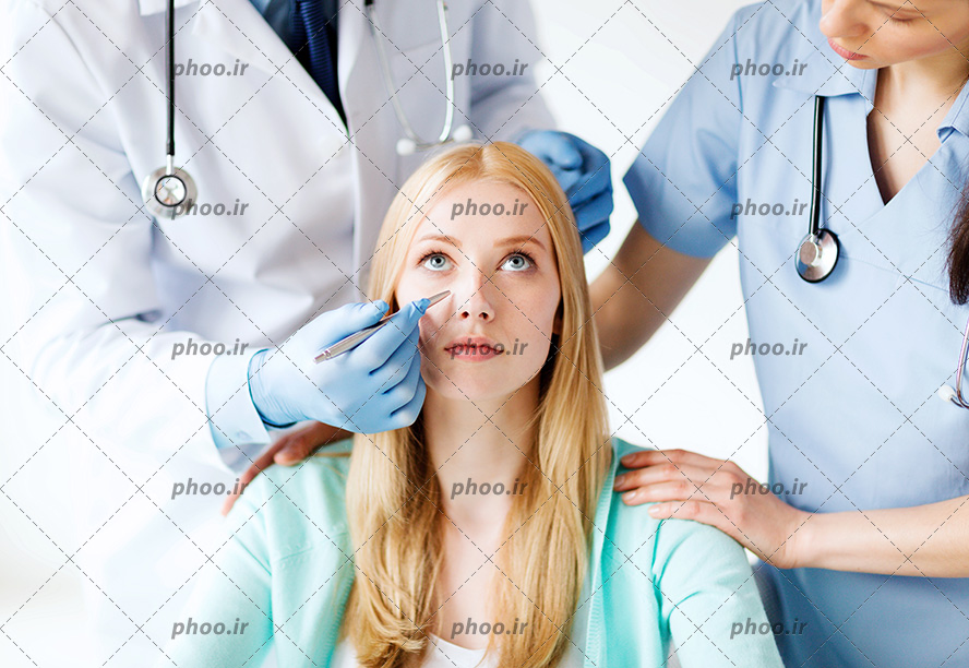 عکس با کیفیت پزشک و پرستار ایستاده در کنار زن و پزشک در حال علامت گذاری صورت زن با خودکار