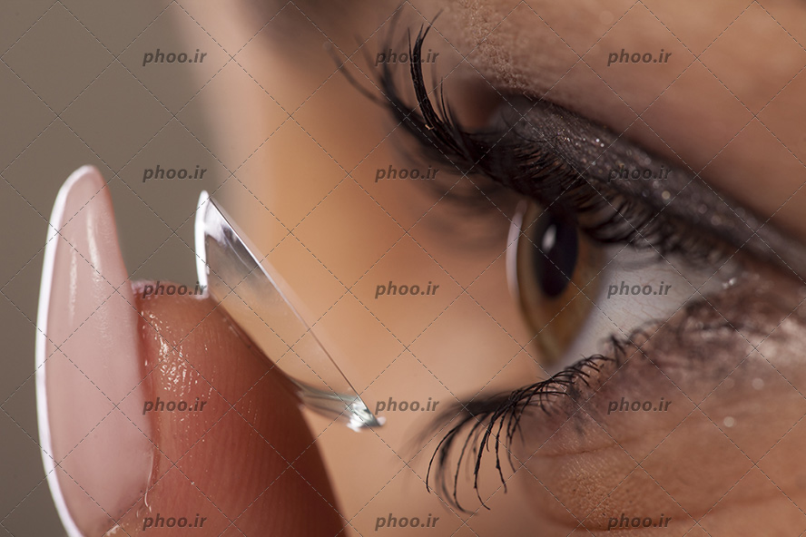 عکس با کیفیت چشم زن به رنگ عسلی و مژه های پر پشت در حال گذاشتن لنز طبی بی رنگ