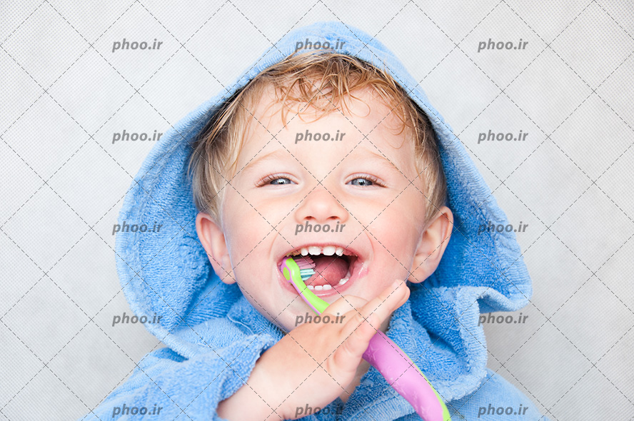 عکس با کیفیت کودک زیبا با چشم های آبی و حوله آبی تنش در حال مسواک زدن