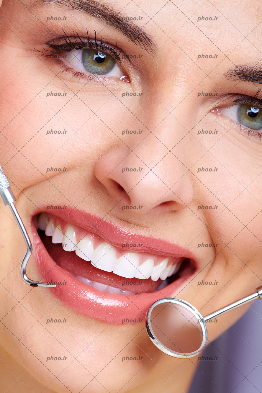 عکس با کیفیت زن زیبا با چشم های سبز جذاب و دندان های منظم و سفید و براق و پزشک در حال معاینه دندان های او