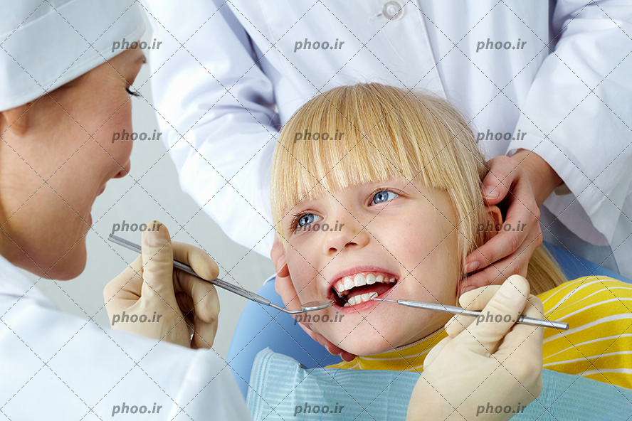 عکس با کیفیت دندان پزشک در حال معاینه دندان های دختر بچه زیبا