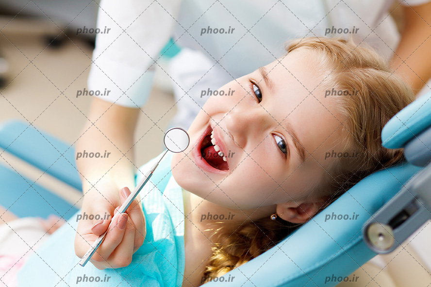 عکس با کیفیت پزشک در حال معاینه دندان های کودک زیبا و کودک در حال خندیدن