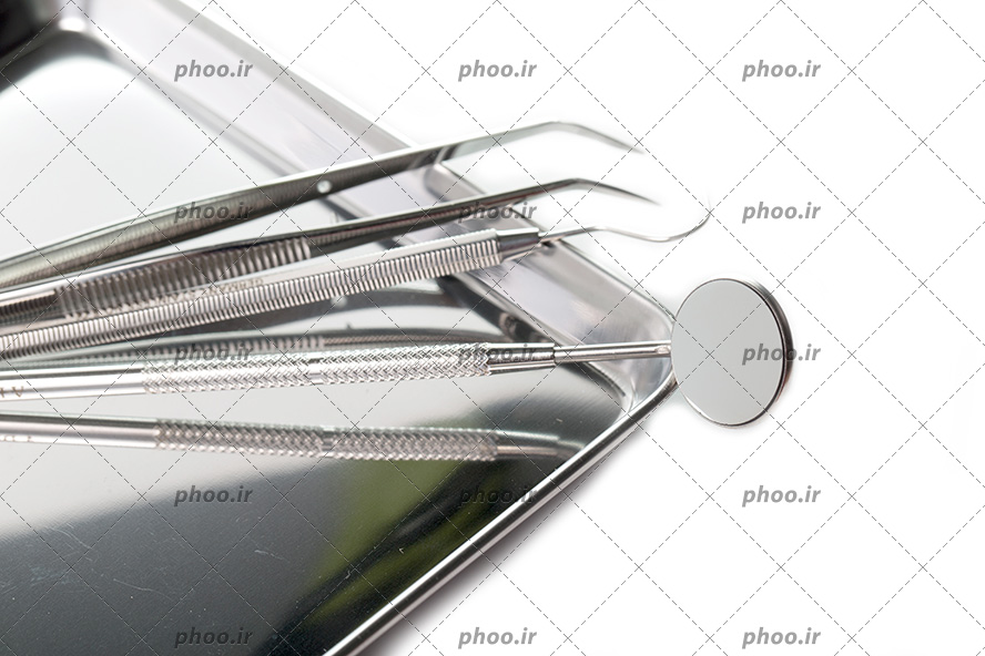 عکس با کیفیت پنس جراحی و سوند دندانپزشکی در کنار آینه مقعر و داخل ظرف فلزی از نمای نزدیک