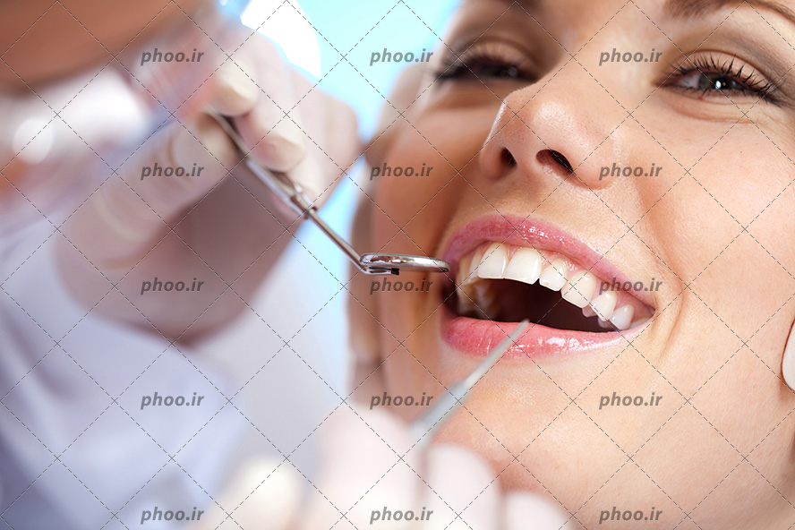 عکس با کیفیت دندانپزشک در حال معاینه کردن دندان های زن زیبا و خندان