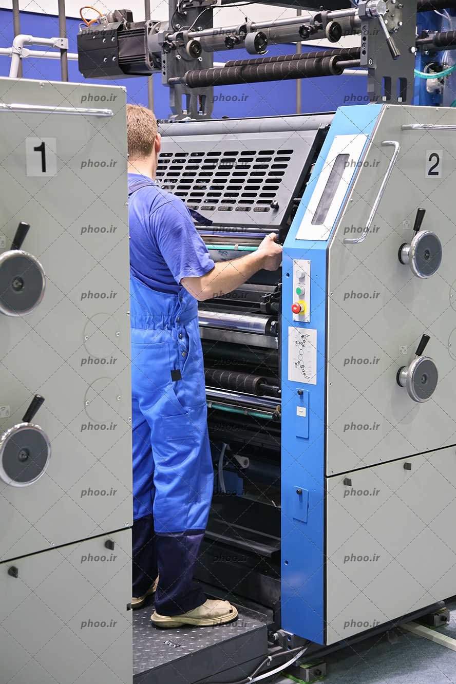 عکس با کیفیت مرد با لباس های آبی مخصوص در حال کار کردن با دستگاه بزرگ چاپ
