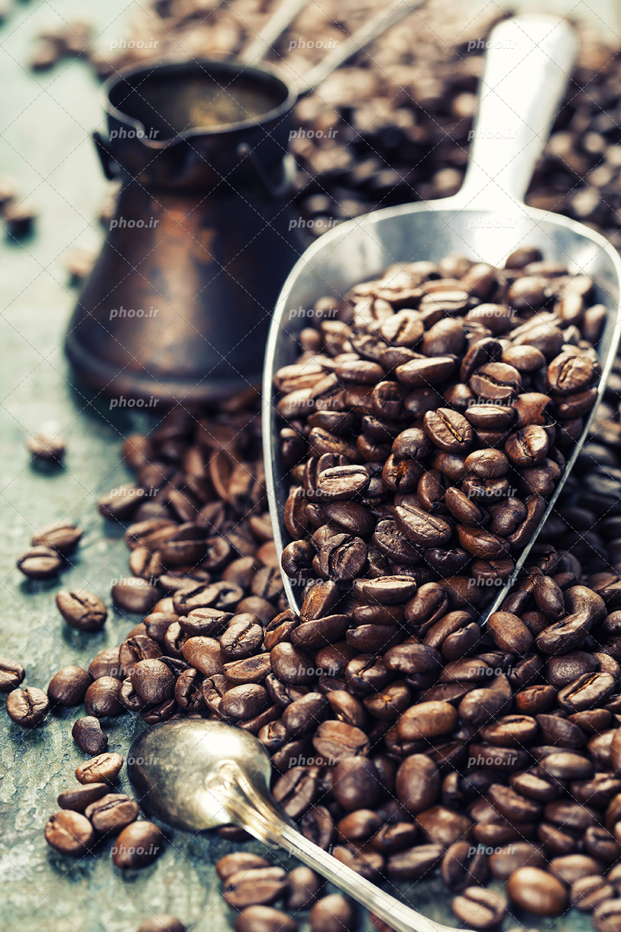 عکس با کیفیت پیمانه ای نقره ای و دانه های قهوه خشک بر روی آن و قهوه جوش در کنار آنها