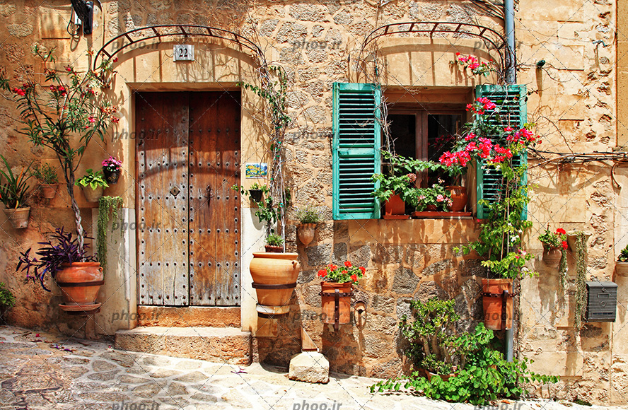 عکس با کیفیت خانه با در چوبی قدیمی و دیوار خانه تزئین شده با گلدان های زیبا و پنجره فیروزه ای