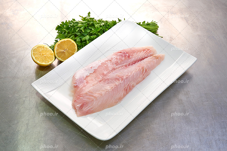 عکس با کیفیت گوشت خام ماهی در ظرف چینی سفید در کنار لیمو ترش ها و جعفری ها