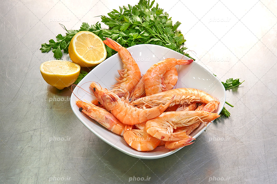 عکس با کیفیت میگو های صید شده در ظزف چینی سفید در کنار لیمو ترش و سبزیجات