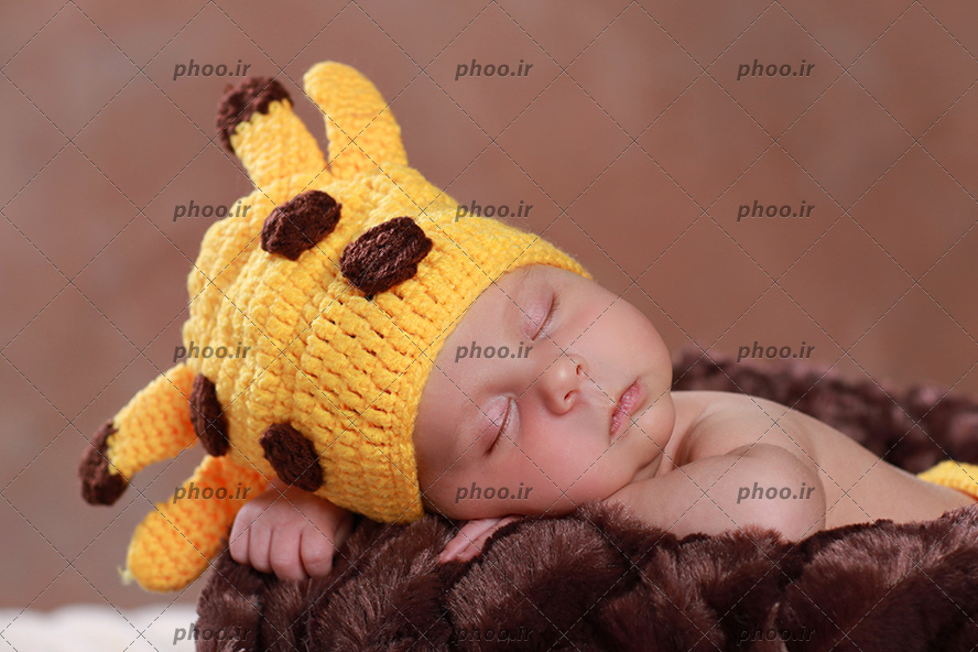 عکس نوزاد ناز در خواب با کلاه زرافه ای روی پتو قهوه ای