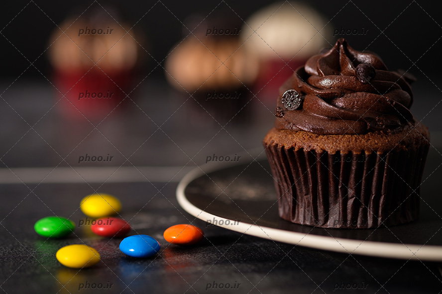 عکس کاپ کیک شکلاتی روی بشقاب و دانه های اسمارتیز روی زمین