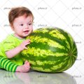 عکس کودک با چشم های آبی و لباس سبز که هندوانه بزرگ را در بغل گرفته است