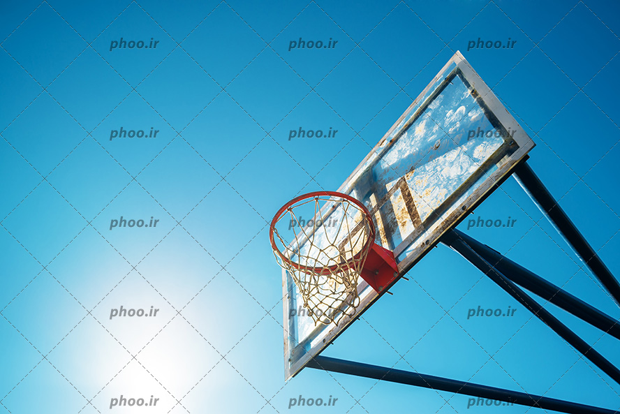 عکس با کیفیت حلقه بسکتبال از نمای پایین و خورشید در آسمان در حال تابیدن