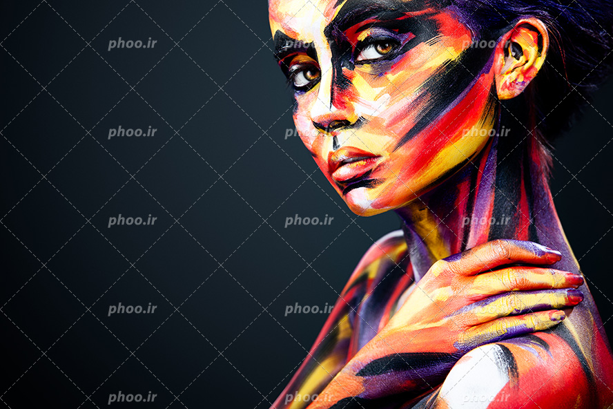 عکس با کیفیت زن با چهره سه رخ و صورت رنگ شده و با ژست دست بر روی شانه ی خود و پس زمینه به رنگ مشکی
