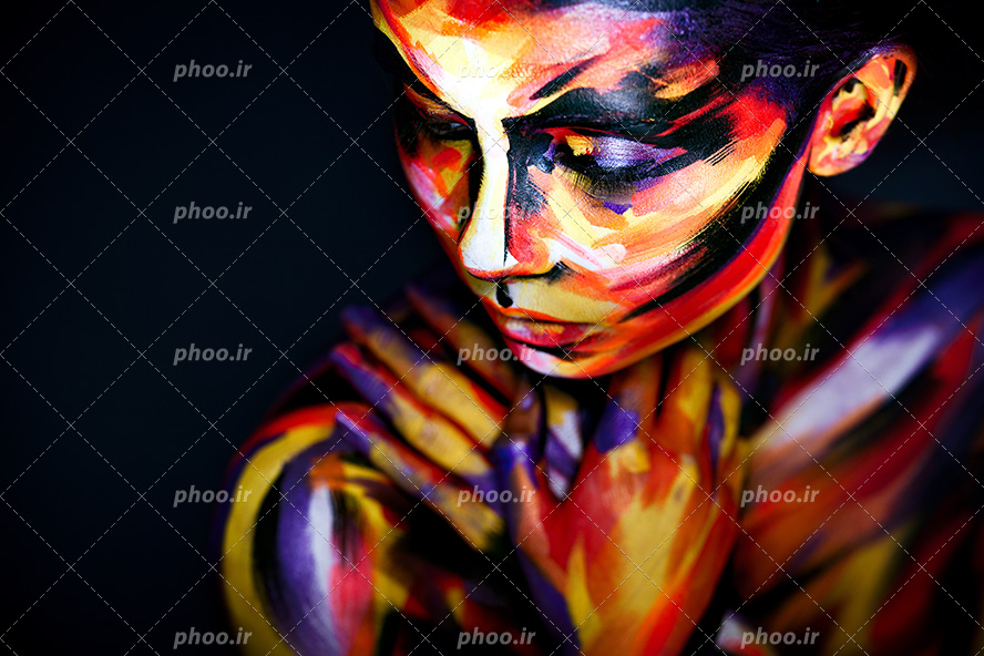 عکس با کیفیت چهره ی زن رو به پایین و صورت نقاشی شده با رنگ های زرد و نارنجی و بنفش و دیگر رنگ ها و پس زمینه به رنگ مشکی