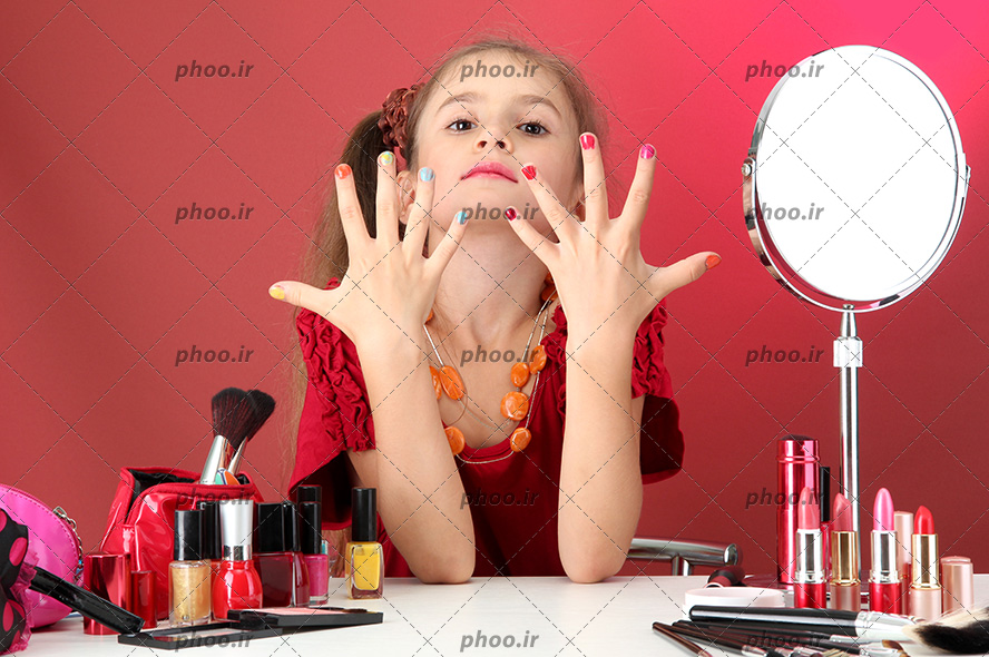 عکس کودک با دست های لاک زده و لوازم آرایش جلویش