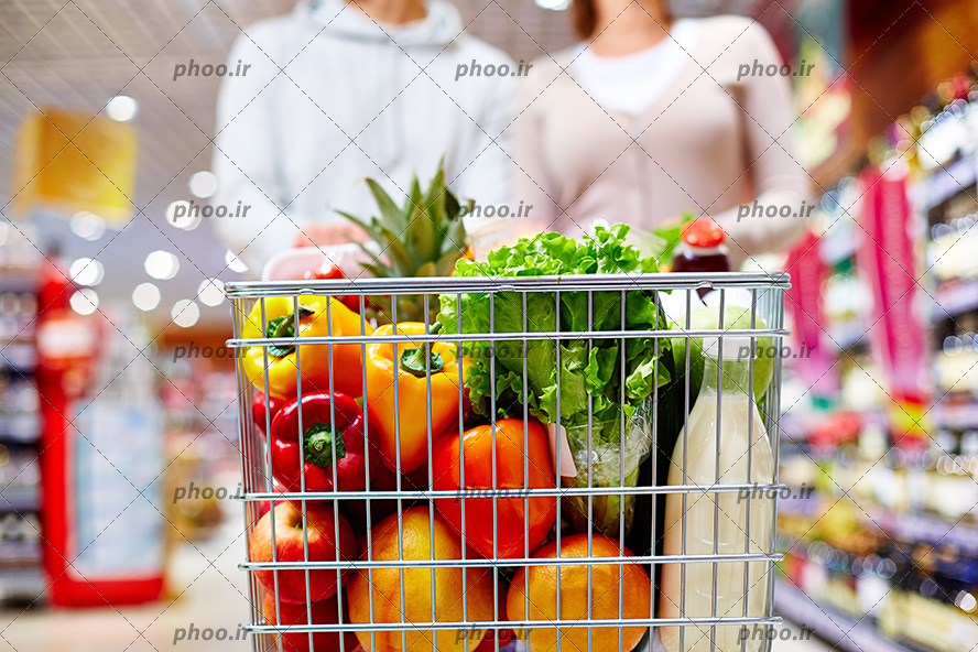 عکس با کیفیت یک زوج با سبد خرید پر از سبزیجات در یک فروشگاه