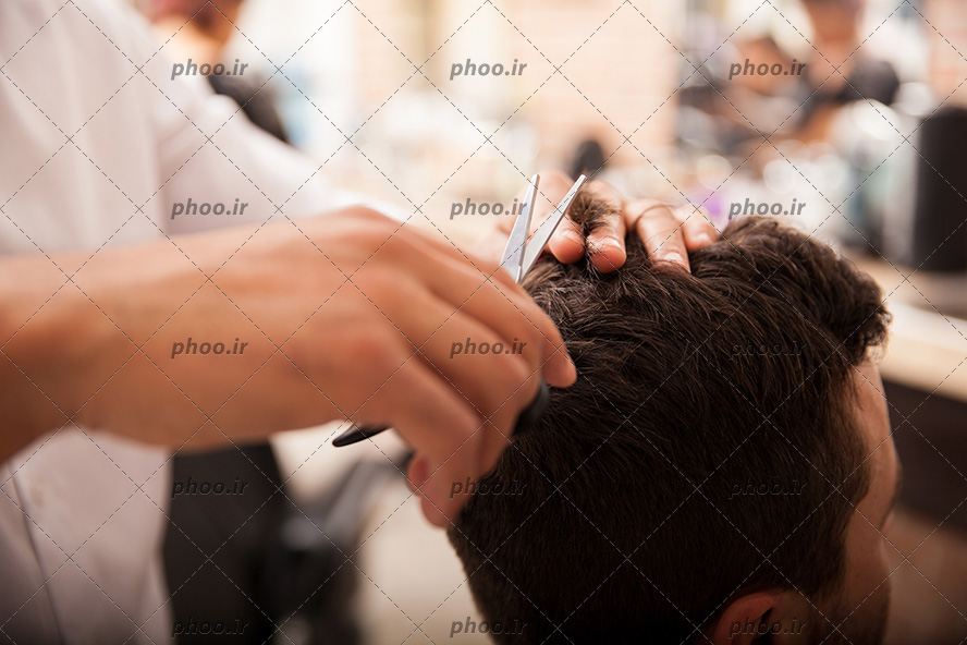 عکس با کیفیت مرد در آرایشگاه در حال کوتاه کردن موهای خود و آرایشگر در حال کات کردن موهای مرد