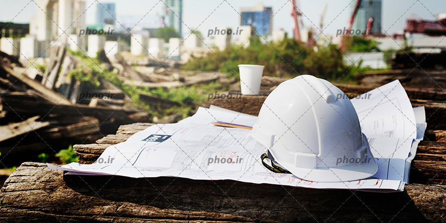 عکس با کیفیت کلاه ایمنی سفید بر روی نقشه های ساختمان و ساختمان های در حال ساخت