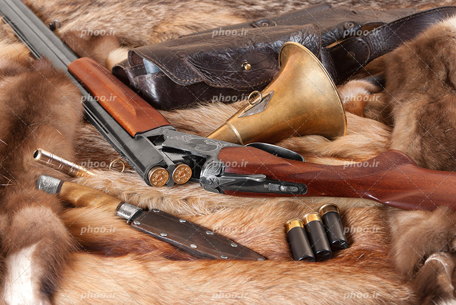 عکس با کیفیت شاتگان در کنار چاقو شکاری و تیر های اسلحه قرار گرفته بر روی پارچه ی پشمی