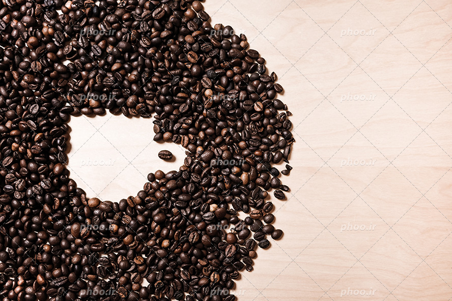 عکس با کیفیت دانه های قهوه در کنار یکدیگر به شکل فنجان بر روی میز چوبی