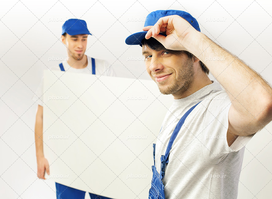 عکس با کیفیت دو مرد تعمیرکار و نصاب دیوار پوش با لباس های مخصوص به رنگ آبی در حال حمل دیوار پوش سفید و در حال لبخند زدن