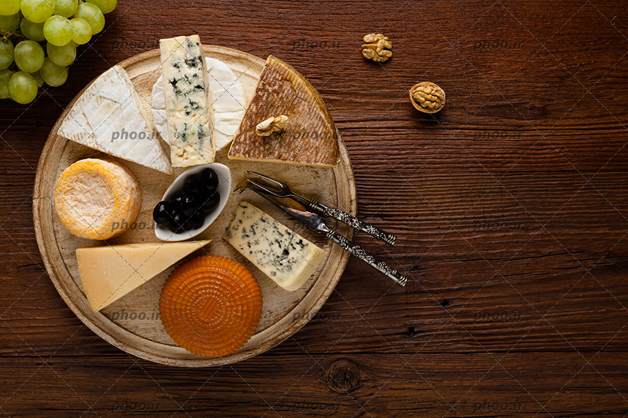 عکس انواع پنیر در کنار گردو و انگور در پس زمینه چوبی