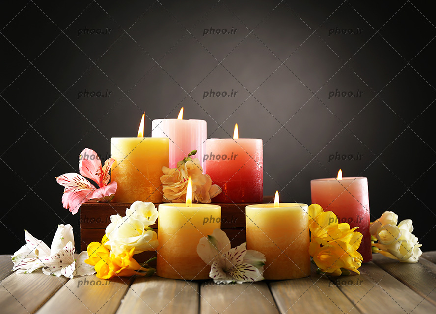 عکس شمع های روشن با رنگ های متفاوت با گل های روی میز در پس زمینه مشکی
