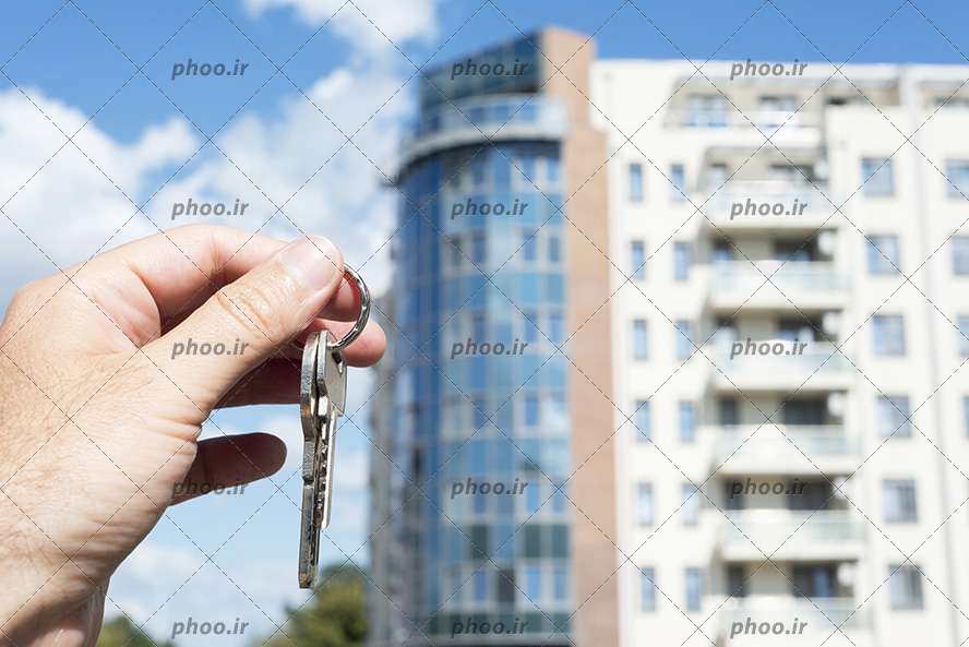 عکس کلید خانه در دست در مقابل آپارتمان