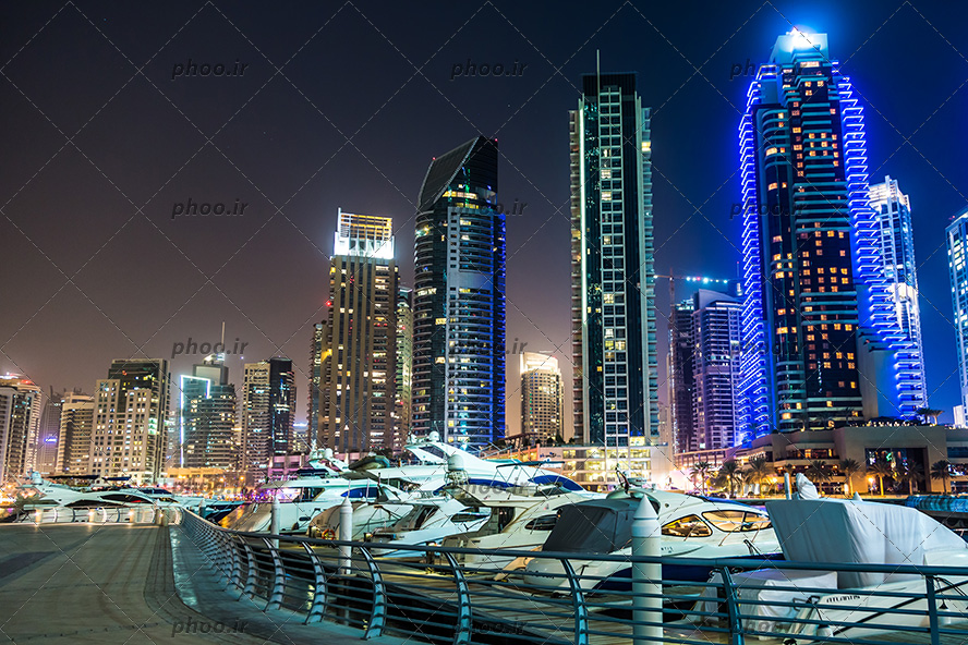 عکس شهر زیبا با برج های نورانی در شب کنار رود یا دریا با قایق ها