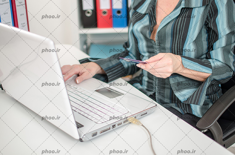 عکس کارت عابر بانک در دست زن جلوی لپ تاپ نشسته